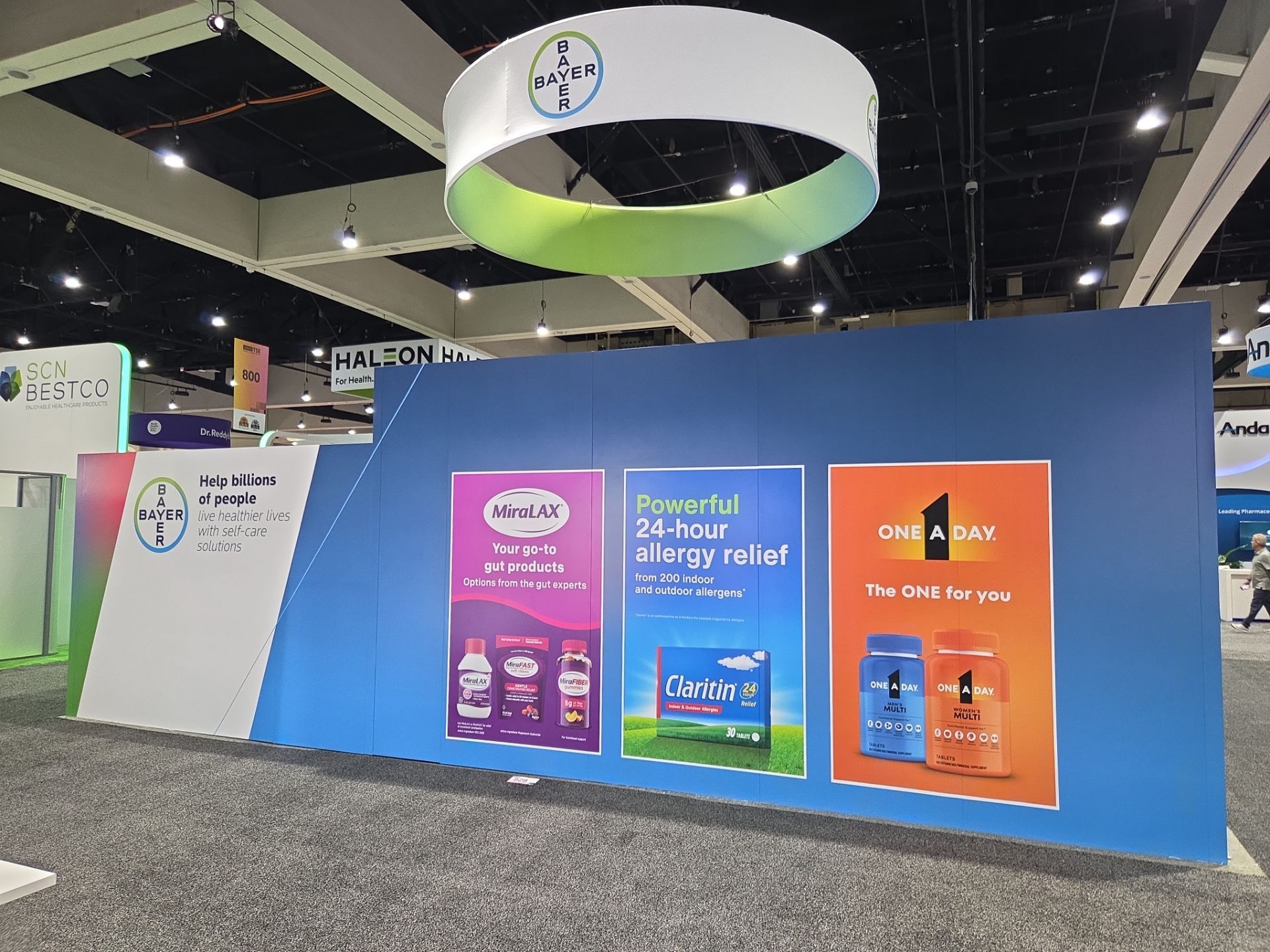 Bayer NACDS booth — front facade with brand graphics wall featuring MiraLAX, Claritin, and One A Day