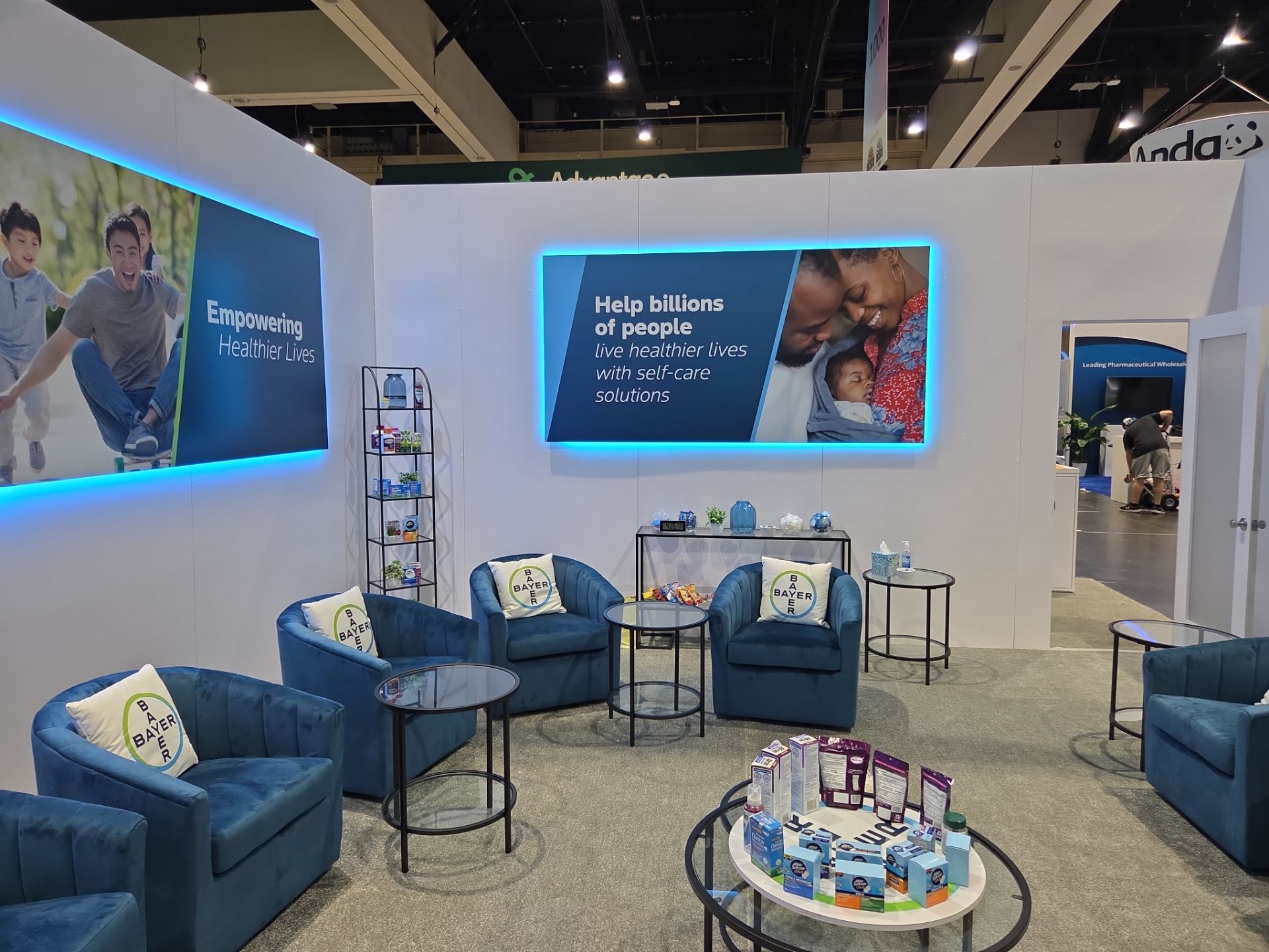 Booth interior — backlit lifestyle panels, branded seating, and product displays on coffee tables