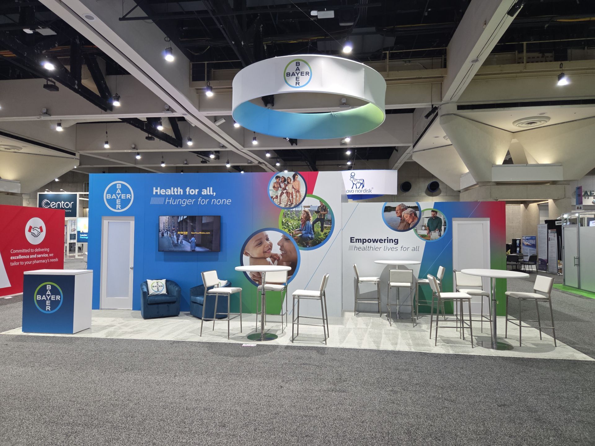 Bayer booth wide view — entrance with lifestyle imagery, Health for All messaging, and high-top meeting tables